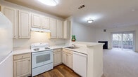 Located at 108 Olde Towne Ave in Gaithersburg, Maryland, this one-bedroom, one-bathroom residence offers a well-organized single-floor layout with a bright, neutral palette throughout. The open-concept kitchen and living area form the heart of the home, where the kitchen features raised-panel cabinetry in a warm cream finish, white appliances including an electric range and dishwasher, a double basin sink, and a peninsula breakfast bar that separates the kitchen from the carpeted living space. The living room is generously proportioned, anchored by a classic wood-burning fireplace and a sliding glass door that provides direct access to an outdoor area, allowing natural light to fill the room. The bedroom is a comfortable, well-sized retreat with plush carpeting and a pair of windows that offer views of the surrounding neighborhood, creating a bright and airy atmosphere. The full bathroom includes a single-vanity with light wood cabinetry, a large mirror, an elegant chandelier-style light fixture, and a full soaking tub with a shower combination, all finished with neutral tile flooring. The consistent use of soft, neutral tones and carpet throughout the living and bedroom areas contributes to a cohesive and welcoming ambiance across the entire residence.