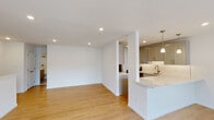 Located at Norwich Gate in East Norwich, NY, this two-floor residence showcases a thoughtfully designed interior with modern finishes and a practical layout. The main level features an open-concept living and kitchen area bathed in recessed lighting, with warm light wood flooring that flows seamlessly throughout. The kitchen is a standout, equipped with shaker-style gray cabinetry, crisp white quartz countertops, a white tile backsplash, stainless steel appliances, and a peninsula with an undermount sink and brushed gold faucet. Pendant lights with antique brass fixtures add a refined touch above the counters. The living area is bright and open, offering a clean, versatile space. A carpeted staircase with white trim leads to the upper level, where hardwood-style flooring continues through the hallway. The upper floor includes a generously sized bedroom with plush carpeting, a built-in closet, and recessed lighting. A full bathroom on this level features large-format gray tile flooring, a wood-toned vanity, a tub-shower combination, and a window that brings in natural light. The overall ambiance throughout the home is clean, contemporary, and move-in ready.