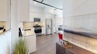 Located in the vibrant West Los Angeles neighborhood of 11311 La Grange, this modern single-floor residence offers a thoughtfully designed open-concept layout with clean lines and a bright, contemporary aesthetic throughout. The living area features rich wood-tone flooring, soaring ceilings with exposed ductwork and industrial-style track lighting, and a dramatic floor-to-ceiling window that floods the space with natural light and provides sweeping views of the surrounding cityscape. The open kitchen is outfitted with sleek flat-front white cabinetry extending to the ceiling, warm countertops, a mosaic tile backsplash, and a full suite of stainless steel appliances including a gas range, microwave, dishwasher, and refrigerator. A dedicated dining area and flexible workspace sit adjacent to the living room, creating a seamlessly connected living environment. The bedroom is a serene retreat featuring plush carpeting, generous natural light from a large window, and ample space for rest and relaxation. The bathroom continues the home's clean, modern palette with mosaic tile flooring, a glass-enclosed shower, and direct access to a walk-in closet with built-in shelving. The unit's all-white walls and abundant recessed lighting contribute to a bright, airy ambiance throughout.