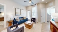 This 2-bedroom, 2-bathroom single-floor residence combines modern finishes with a functional, open layout. The combined kitchen and living area serves as the heart of the home, featuring light wood-style flooring throughout. The kitchen is outfitted with crisp white cabinetry, a subway tile backsplash, stainless steel appliances — including a refrigerator, range, and microwave — and a granite-topped island with bar seating, ideal for casual dining or entertaining. The adjoining living room is bright and welcoming, with large windows fitted with blinds that allow ample natural light, a ceiling fan with a light fixture, and direct access to the outdoors via a glass-panel door. Both bedrooms are comfortably sized, each offering large windows with outdoor views and light wood-style flooring. The primary bedroom connects to a spacious walk-in closet with dual hanging rods. The two bathrooms each feature granite vanity countertops, white cabinetry, and a tub-shower combination. One bathroom includes a rustic wood floating shelf, adding a warm accent. Neutral, light tones are used consistently throughout, contributing to a clean, cohesive, and modern aesthetic across the entire residence.