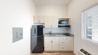 This single-floor unit offers a clean, modern interior designed for efficient and comfortable living. The kitchenette is thoughtfully equipped with light wood cabinetry providing ample upper and lower storage, granite-style countertops, a stainless steel sink, a built-in cooktop, a microwave set within a dedicated niche, and a full-size black refrigerator — all arranged in a compact, well-organized layout atop wood-look flooring.

The main living area features warm wood-look flooring that extends throughout the space, complemented by a two-tone color scheme of crisp white walls and a bold charcoal accent wall that adds depth and visual interest. A window fitted with horizontal blinds allows natural light to filter in, while a wall-mounted PTAC unit ensures year-round climate control.

The bathroom is finished with the same attention to detail, showcasing a granite-top vanity with an undermount sink and chrome fixtures, a large mirror with an integrated medicine cabinet offering additional storage, and open shelving for easy access to essentials. White walls and clean lines give the bathroom a bright, fresh feel.

Overall, the space presents a cohesive, contemporary aesthetic with practical finishes suited for functional, everyday living.