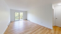 Located at 530 Proudfoot Lane in London, Ontario, this one-bedroom, one-bathroom unit offers a well-organized and functional layout finished with warm light hardwood flooring throughout. The open kitchen and living area form the heart of the space, where the kitchen is equipped with white cabinetry extending to the ceiling, stainless steel appliances including a full-size refrigerator and dishwasher, a dark countertop, and classic subway tile backsplash. The living area is generously proportioned with clean white walls and a large sliding glass door that opens to a balcony, flooding the room with natural light and offering pleasant views of surrounding greenery. The bedroom is a comfortable, well-sized room featuring a built-in double closet, a window with tree-lined views, and baseboard heating. The bathroom is finished to a modern standard, featuring large-format white wall tiles surrounding a full soaker tub with shower, a stone-topped vanity with an undermount sink, a large mirror, and tile flooring. Throughout the unit, the crisp white walls and consistent hardwood flooring create a bright, cohesive aesthetic that is both practical and inviting.