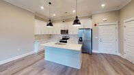 Located at 1154 Westyn Village Way in Forest, Virginia, this single-story home is designed with a clean, modern aesthetic that emphasizes open living and functional design. The layout connects the kitchen and living areas seamlessly, creating a spacious, airy feel throughout the main living space.

The kitchen is a standout feature, showcasing white shaker-style cabinetry with sleek hardware, light quartz countertops, and a marble-style tile backsplash. A center island with an undermount sink and pendant lighting serves as a focal point, while stainless steel appliances—including a French door refrigerator, electric range, and over-the-range microwave—complete the space. Recessed lighting and crown molding add polished finishing touches.

The living area extends naturally from the kitchen, featuring wood-look plank flooring, crown molding, a ceiling fan, and windows that invite natural light. Access to an outdoor area is visible, enhancing the sense of openness.

The bathroom is well-appointed with a white vanity, quartz countertop, a tub-shower combination with white surround, and wood-look tile flooring in warm neutral tones. Neutral gray-beige wall tones carry throughout the home, contributing to a cohesive and contemporary atmosphere.