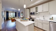 This single-story residence is designed with an open, flowing layout that connects key living areas seamlessly. The kitchen serves as a central hub, featuring white shaker-style cabinetry, subway tile backsplash, stainless steel appliances including a range and built-in microwave, and a large center island with white quartz countertops illuminated by pendant lighting. Wood-look flooring runs throughout, adding warmth and continuity across the space.

The living room is generously proportioned, bathed in natural light from oversized windows dressed with floor-length drapes. Crown molding and a ceiling fan contribute to the room's polished finish, while direct access to an outdoor balcony enhances the sense of openness.

The bedrooms offer comfortable retreats, each featuring wood-look flooring, crown molding, and large windows. One bedroom provides balcony access, further extending the connection to the outdoors. The primary suite includes an expansive walk-in closet with multi-tier wire shelving systems offering abundant storage.

The primary bathroom features a long dual-sink vanity with white countertops, ample cabinetry, light tile flooring, and direct access to the walk-in closet, creating a practical and cohesive suite arrangement throughout.