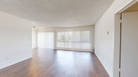 This 3-bedroom, 2-bathroom single-story home in Long Beach, California offers a practical and well-organized layout. The living and dining area is bright and welcoming, featuring rich hardwood-style flooring, a textured ceiling, and expansive windows dressed with vertical blinds that invite generous natural light and outdoor views. A ceiling fan adds comfort to the space. The galley-style kitchen is efficiently designed with white shaker cabinetry, speckled granite-look countertops, a double-basin stainless steel sink, an electric cooktop, a dishwasher, and a window that brings in additional light. The primary bedroom offers a comfortable footprint with plush carpeting, a sliding-door closet with built-in hanging rods, and a window with vertical blinds. Additional bedrooms include a mix of hardwood-style and carpeted flooring, each with windows providing natural light. The bathrooms are clean and functional, featuring chrome hardware accents. A hallway connects the bedrooms and bathrooms, maintaining a smooth flow throughout the home. Crisp white walls and a consistent neutral palette give the entire residence a clean, move-in-ready feel suited for comfortable everyday living.