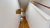 This two-story home offers a well-organized layout spread across two floors, combining functional design with warm, inviting finishes throughout. Warm-toned hardwood-style flooring flows consistently through every room, tying the space together cohesively.

The main level features an open kitchen and living room area. The kitchen is equipped with gray shaker-style cabinetry, white countertops, stainless steel appliances including a refrigerator, range, and dishwasher, and a window above the sink that brings in natural light. The adjacent living room is bright and open, with a ceiling fan, a front-facing window with exterior views, and direct access to the entry door.

Upstairs, the primary bedroom stands out with vaulted ceilings, a ceiling fan, and an airy feel. A dedicated walk-in closet with built-in shelving and a hanging rod provides generous storage. The upper floor also includes two additional bedrooms and a full bathroom outfitted with a soaking tub and shower combination. A second bathroom on the lower level features a vanity with cabinetry and clean, minimal finishes.

A long, well-lit hallway connects the upper-level rooms, with a staircase featuring a warm wood handrail providing easy access between floors. Throughout the home, white walls and clean trim create a bright, neutral backdrop ready for personalization.