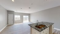 This single-floor residence is designed with a clean, contemporary aesthetic defined by a neutral gray and white color palette throughout. The open-concept layout connects the kitchen and living area seamlessly, creating a spacious and airy feel. The kitchen is a standout feature, showcasing striking dark granite countertops with dramatic veining, crisp white shaker-style cabinetry with brushed gold hardware, and a double basin undermount sink set within a central island. Ample upper and lower cabinetry provides generous storage and functional counter space.

The living area benefits from abundant natural light streaming through large windows and sliding glass doors fitted with vertical blinds, which open to an outdoor balcony. Light wood-look flooring runs throughout the main living spaces, complementing the soft gray walls and clean white trim.

The bedrooms are well-proportioned, each featuring light wood flooring, recessed lighting, and built-in closets with rod and shelf systems. The bathrooms maintain the same design language, with matching granite vanity tops, white cabinetry, and neutral tile flooring. The full bathroom includes a walk-in tiled shower with a built-in niche and coordinating floor tile, offering a polished, functional finish throughout.