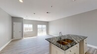 This single-floor residence is designed with a clean, contemporary aesthetic defined by a neutral gray and white color palette throughout. The open-concept layout connects the kitchen and living area seamlessly, creating a spacious and airy feel. The kitchen is a standout feature, showcasing striking dark granite countertops with dramatic veining, crisp white shaker-style cabinetry with brushed gold hardware, and a double basin undermount sink set within a central island. Ample upper and lower cabinetry provides generous storage and functional counter space.

The living area benefits from abundant natural light streaming through large windows and sliding glass doors fitted with vertical blinds, which open to an outdoor balcony. Light wood-look flooring runs throughout the main living spaces, complementing the soft gray walls and clean white trim.

The bedrooms are well-proportioned, each featuring light wood flooring, recessed lighting, and built-in closets with rod and shelf systems. The bathrooms maintain the same design language, with matching granite vanity tops, white cabinetry, and neutral tile flooring. The full bathroom includes a walk-in tiled shower with a built-in niche and coordinating floor tile, offering a polished, functional finish throughout.