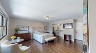 This single-floor unit offers a thoughtfully designed layout that balances comfort and functionality. The generously sized bedroom is a standout feature, showcasing rich dark hardwood floors, neutral gray walls, and abundant natural light from a large window. A tufted upholstered bed with nail-head trim serves as the room's centerpiece, complemented by dark wood dressers and nightstands. A mirrored sliding closet provides ample storage, while a wall-mounted TV adds modern convenience. A tufted bench and accent chair complete the inviting atmosphere.

The kitchen is clean and contemporary, featuring white cabinetry, light quartz countertops, and a classic white subway tile backsplash with dark grout. A deep stainless steel sink paired with a matte black pull-down faucet adds a stylish contrast to the bright, crisp finishes.

The bathroom is fully updated with floor-to-ceiling white subway tile surrounding a soaking tub and shower combo. A white vanity with a taupe quartz countertop, an undermount sink, and a mirrored medicine cabinet contribute to the polished look. Wood-look porcelain tile flooring extends throughout the bathroom and into a dedicated laundry area, which houses a stacked washer and dryer unit for added convenience.