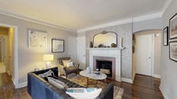 This well-appointed single-floor residence seamlessly combines classic character with contemporary updates throughout its thoughtfully arranged layout. The living room serves as the heart of the home, anchored by a decorative brick fireplace framed by an elegant white mantel and complemented by ornate patterned wallpaper and an arched mirror above. Crown molding lines the ceiling, and rich hardwood flooring runs throughout the main living areas, adding warmth and sophistication. A tufted leather sofa and eclectic accent chairs complete the inviting atmosphere.

The open living and dining area extends toward a bay of multi-pane windows dressed in sheer curtains, flooding the space with natural light and creating an airy, expansive feel. The kitchen is efficiently designed with white shaker cabinetry, light stone countertops, a subway tile backsplash, and a full suite of stainless steel appliances including a gas range, refrigerator, and dishwasher.

The bedroom offers a serene retreat with plush carpeting, a statement textured accent wall behind the bed, and a generous closet. A dedicated home office provides a quiet workspace with crown molding details and a built-in niche. The bathroom features classic mosaic tile flooring, white subway tile walls, and a soaking tub, rounding out this character-rich residence.