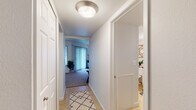 This single-floor residence offers a thoughtfully designed layout that balances comfort and practicality throughout its interconnected spaces. The living room is carpeted and bathed in a neutral palette, providing a relaxed setting anchored by clean white walls that complement the understated décor.

Adjacent to the living area, a dedicated dining nook features an elegant chandelier overhead and a pass-through window connecting directly to the kitchen, making entertaining and daily meals convenient. The galley-style kitchen is well-equipped with stainless steel appliances, including a range with over-the-range microwave, dark granite countertops, and ample white cabinetry providing generous storage. Light tile flooring runs throughout the kitchen and extends into the hallway.

A tiled corridor connects the main living spaces to the private areas of the residence. The bedroom is carpeted and tranquil, benefiting from natural light through a window and featuring a walk-in closet for substantial storage. The full bathroom includes a wide vanity with granite countertops, white cabinetry, tile flooring, and a tub-shower combination, completing the functional and cohesive design of this residence.