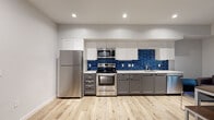 This single-floor residence in the Berkeley, CA area offers a thoughtfully designed layout with a blend of modern finishes and functional living spaces. The kitchen serves as a standout feature, showcasing two-tone cabinetry with white upper cabinets and charcoal gray lower cabinets, a bold cobalt blue subway tile backsplash, and a full suite of stainless steel appliances including a refrigerator, electric range, and over-the-range microwave. Light wood-look flooring runs throughout the kitchen and common areas, adding warmth to the contemporary aesthetic. Recessed lighting provides even, bright illumination throughout. The living area offers a comfortable, flexible space with a window that invites natural light, suitable for lounging or dining. The bedrooms are carpeted for comfort and include ceiling fans and windows with blinds, with one room configured to accommodate two beds and dual workstations. The bathroom features a clean, all-white design with a soaking tub and shower combination, white vanity, and matching light wood flooring. A dedicated vanity area with in-unit washer and dryer adds everyday convenience. The overall ambiance is clean, modern, and move-in ready.