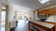 This well-designed single-floor residence offers a thoughtfully laid-out interior that blends contemporary style with everyday functionality. The open-concept kitchen and living area serves as the heart of the home, where rich hardwood flooring, recessed lighting, and a prominent skylight work together to create a bright, welcoming atmosphere. The kitchen is outfitted with warm wood cabinetry, stainless steel appliances including a refrigerator, range, and microwave, complemented by a clean tile backsplash and a freestanding island with a neutral countertop surface that provides both prep space and casual seating potential.

The living area flows seamlessly from the kitchen, receiving generous natural light through large sliding glass doors that open to an outdoor view, further enhancing the sense of openness. The bedroom is a calm, carpeted retreat with a dedicated window framing an exterior view, allowing ample daylight to filter in.

Two bathrooms serve the unit: one features a glass-enclosed walk-in shower with built-in shelving and tile flooring, while the second includes a full soaking tub and shower combination, a wood-toned vanity, and light tile floors. Throughout, the neutral color palette and clean architectural lines create a cohesive, modern ambiance.