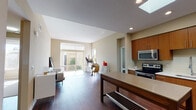 This well-designed single-floor residence offers a thoughtfully laid-out interior that blends contemporary style with everyday functionality. The open-concept kitchen and living area serves as the heart of the home, where rich hardwood flooring, recessed lighting, and a prominent skylight work together to create a bright, welcoming atmosphere. The kitchen is outfitted with warm wood cabinetry, stainless steel appliances including a refrigerator, range, and microwave, complemented by a clean tile backsplash and a freestanding island with a neutral countertop surface that provides both prep space and casual seating potential.

The living area flows seamlessly from the kitchen, receiving generous natural light through large sliding glass doors that open to an outdoor view, further enhancing the sense of openness. The bedroom is a calm, carpeted retreat with a dedicated window framing an exterior view, allowing ample daylight to filter in.

Two bathrooms serve the unit: one features a glass-enclosed walk-in shower with built-in shelving and tile flooring, while the second includes a full soaking tub and shower combination, a wood-toned vanity, and light tile floors. Throughout, the neutral color palette and clean architectural lines create a cohesive, modern ambiance.