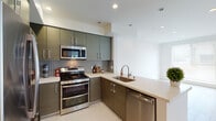 Located on Hollywood Boulevard in Los Angeles, this single-floor residence showcases a clean, modern design aesthetic throughout. The kitchen is a standout feature, equipped with stainless steel appliances including a double-oven gas range, built-in microwave, and dishwasher. Textured flat-panel cabinetry in a warm gray-brown tone pairs with light countertops and a sleek tile backsplash, creating a polished, contemporary look. Light ceramic tile flooring completes the space.

The open living area features light wood-look flooring, recessed lighting, and bright white walls, lending an airy, spacious feel. Large vertical blinds allow for natural light control. Bedrooms are carpeted and feature ample natural light through windows with blinds, with one bedroom offering sliding glass door access to an outdoor area.

The primary bathroom is well-appointed with a double-sink vanity, a glass-enclosed shower, and a soaking tub, all finished in neutral tile and clean-lined fixtures. Additional bathrooms include modern vanities with vessel or undermount sinks, large mirrors, and consistent tile flooring, maintaining a cohesive and sophisticated design throughout the residence.