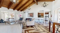 Located at 8310 E McDonald Dr in Scottsdale, Arizona, this single-floor space offers a well-appointed and visually distinctive interior defined by standout architectural details. The most eye-catching feature is the dramatic vaulted ceiling with exposed wood beams, lending a warm, rustic-modern character throughout the main living area. Complementing this overhead craftsmanship is a bold multi-tone herringbone hardwood floor that flows seamlessly across the entire space, adding depth and visual interest underfoot.

The open living area is generously sized, accommodating multiple seating arrangements, a wall-mounted television, and a full-size pool table—making it well-suited for both relaxed gatherings and active recreation. Elegant iron-and-crystal chandeliers illuminate the vaulted section, while large windows and glass doors on multiple walls flood the interior with natural light and offer views of the lush, landscaped outdoor surroundings, including glimpses of a pool area.

The kitchen is accessible via a pass-through bar counter with seating for two, and is equipped with stainless steel appliances including a range, microwave, refrigerator, and a dedicated ice maker. A skylight above the kitchen adds additional natural brightness. A separate arched alcove provides an intimate lounge corner, further enhancing the spatial variety of this thoughtfully designed Scottsdale property.