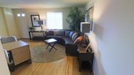 This three-floor residence offers a well-organized and comfortable layout spread across multiple levels, providing ample space for everyday living. The living area is a welcoming focal point, featuring warm hardwood floors that run throughout and a large sectional sofa perfectly positioned to encourage relaxation and conversation. A circular area rug anchors the seating arrangement, while generous natural light streams in through bright windows, creating an airy and open atmosphere. Tasteful decor, including framed artwork, ambient table lamps, and lush indoor greenery, adds character and warmth to the space. A wooden console table serves a dual purpose as both a decorative and functional element near the seating area. The neutral wall tones complement the natural wood floors, contributing to a cohesive and calming aesthetic throughout. With three full floors, this home offers versatility and room to accommodate a variety of living needs, from private retreats on the upper levels to shared gathering spaces on the main floor. The overall ambiance is warm, livable, and well-maintained, making it an ideal space for those seeking both comfort and practicality in a multi-level home.