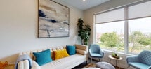 This thoughtfully designed single-floor residence at 222 Avenue E in Bayonne, NJ offers a seamless blend of modern aesthetics and functional living. The living area is bright and welcoming, featuring warm neutral tones, hardwood-style flooring, and large windows that frame outdoor greenery and neighborhood views. A statement abstract artwork anchors the space above a tufted cream sofa accented with vibrant teal and gold throw pillows, creating an inviting and stylish atmosphere.

The kitchen is outfitted with contemporary two-tone cabinetry — rich dark wood lowers paired with warm taupe uppers — complemented by white quartz countertops and a marble-effect backsplash. Stainless steel appliances, including a gas range and built-in microwave, complete this functional and elegant cooking space.

The bedrooms are generously proportioned, each featuring large windows that allow abundant natural light and views of the surrounding greenery. Dark hardwood floors, neutral wall tones, and thoughtful furnishings lend each room a calm, restful quality.

The bathrooms are finished to a high standard, showcasing large-format tile flooring, full marble-effect wall tiling, floating dark-wood vanities with white basins, round mirror accents, and warm brass or chrome fixtures — delivering a clean, spa-like aesthetic throughout.