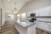 This thoughtfully designed two-story home offers three bedrooms, four bathrooms, and a functional layout spread across two floors. The main level features a bright, open-concept kitchen and living area anchored by soaring vaulted ceilings that amplify the sense of space. The kitchen is equipped with white shaker cabinetry, granite countertops, stainless steel appliances, a subway tile backsplash, and a central island with a built-in sink — all set atop warm hardwood-style flooring. A door off the living area opens directly to an outdoor deck. A powder room with a pedestal sink and hardwood flooring serves guests on this level conveniently. A striking staircase with sleek black metal railings connects the floors. The upper level hosts the primary bedroom and additional bedrooms, each featuring plush carpeting, vaulted ceilings, and generous closets outfitted with wire shelving systems. A dedicated laundry room with a full-size washer and dryer adds everyday convenience. The lower level includes carpeted bedrooms with slim horizontal windows that allow natural light, along with utility rooms and hallways. Neutral warm-toned walls throughout lend a clean, contemporary feel to every room.
