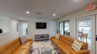 This single-floor clubhouse is thoughtfully designed to serve as a functional and stylish community gathering space. The interior is anchored by a bright, open-plan layout finished with warm hardwood-style flooring and clean white walls throughout.

The lounge area offers comfortable seating with tufted caramel leather sofas arranged around a patterned area rug, complemented by a wall-mounted flat-screen TV and a media console. Large sliding glass doors provide direct access to an outdoor patio area, allowing natural light to flow in and offering views of the exterior seating space beyond.

A distinctive architectural detail separates the lounge from the adjacent areas — a half-wall ledge lined with lush indoor planters and a row of arched windows that frame greenery and let in abundant natural light. A modern pendant chandelier hangs above, adding an elegant touch.

The kitchen is fully equipped with stainless steel appliances, including a refrigerator, range, built-in microwave, and dishwasher. White shaker cabinetry, quartz countertops, and a vibrant patterned mosaic tile backsplash give the kitchen a lively yet polished character. Adjacent dining tables with contemporary chairs provide ample seating for group meals or events, making this clubhouse a versatile and inviting space for community use.