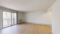 This well-organized 2-bedroom, 1-bathroom residence offers a practical and comfortable layout across a single floor. The two living areas are bright and open, featuring light hardwood-style flooring, neutral white walls, and baseboard heating. One of the living spaces includes a sliding glass door that opens to a balcony with outdoor views, allowing natural light to fill the room, while a wall-mounted air conditioning unit provides additional climate control. A second living area is accessed via an iron-railed staircase and shares the same clean hardwood flooring and neutral palette. The kitchen is efficiently laid out with warm oak cabinetry, dark granite-style countertops, and white appliances including a range, dishwasher, and refrigerator, complemented by a double sink. Both bedrooms are carpeted for comfort and each features its own closet with built-in shelving for ample storage. The bathroom is finished with hardwood-style flooring, white cabinetry with overhead storage, and brushed nickel hardware. A connecting hallway ties the spaces together cohesively. Throughout the unit, the clean, neutral finishes create a bright and functional living environment.