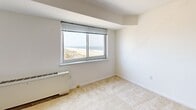 Located at 385 Ocean Blvd in Long Branch, NJ, this single-floor unit offers a well-utilized layout that includes a combined kitchen and living area, one full bathroom, a dedicated entrance, and three closets for ample storage. The open-plan kitchen and living room share a seamless flow, with the kitchen outfitted with warm wood cabinetry spanning the full length of the wall, a gas cooktop, wall oven, refrigerator, and a single-basin sink set on tile flooring. The living area transitions to soft carpeting, creating a comfortable, cohesive space. Windows throughout the unit are a defining feature, with views that stretch across the Atlantic Ocean and Long Branch's sandy beach on one side, and city rooftop views on the other, flooding the space with natural light. The bathroom is clean and functional, featuring a full-size soaking tub with an overhead shower. Bright white walls and neutral tones give the entire unit a fresh, airy ambiance. The entrance hallway includes louvered closet doors, adding classic architectural detail. Baseboard heating units are present in the main living spaces, ensuring year-round comfort. Overall, the unit presents a practical and well-organized coastal living space with notable oceanfront views.