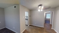 This single-story space offers a consistent, cohesive aesthetic throughout, characterized by neutral gray walls, dark wood-look flooring, and white trim that together create a clean, understated interior. The open living and dining area is connected by a ceiling fan with integrated lighting, providing both function and airflow. A partial wall separates the living space from the kitchen access, adding subtle architectural definition without closing off the layout.

The galley-style kitchen is efficiently organized, featuring white shaker-style cabinetry on both sides, dark speckled countertops, a stainless steel double sink, and black appliances including a refrigerator and range. A flush-mount ceiling light brightens the workspace.

The bedrooms are comfortably sized, each equipped with a ceiling fan and natural light provided by windows fitted with horizontal blinds. The dark flooring carries consistently through these rooms, reinforcing the uniform design language.

Two bathrooms serve the unit. The larger bathroom includes a wide vanity with dual sinks, dark countertops, a large framed mirror, a three-bulb vanity light, and a tiled shower-tub combination. The second bathroom features a single-sink vanity with matching countertops and a framed mirror. Both bathrooms display textured ceilings consistent with the rest of the space.