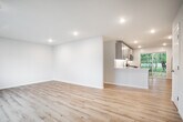 Located at 61 Piedmont Dr in Port Jefferson Station, NY, this single-floor residence has been thoughtfully renovated with clean, contemporary finishes throughout. Light hardwood flooring runs through the main living and kitchen areas, creating a cohesive and airy feel across the open layout.

The kitchen is a standout feature, equipped with gray shaker-style cabinetry, crisp white quartz countertops, a white subway tile backsplash, and stainless steel appliances including a gas range, microwave, dishwasher, and refrigerator. A peninsula provides additional prep space and casual seating potential. A sliding glass door and a large window allow natural light to pour in while offering views of the surrounding greenery.

The open-concept living area flows naturally from the kitchen, separated by a partial wall that defines each zone while maintaining a connected feel. Recessed lighting is installed throughout, providing consistent illumination.

The bedrooms offer comfortable proportions, with some featuring plush carpeting and generous closet space, including double closets with built-in racking. The bathroom presents a clean, modern aesthetic with a tiled tub-surround, a wood-toned vanity with a white countertop, and a window for natural ventilation. Baseboard heating is present throughout the home.