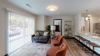 This single-floor residence offers a well-organized layout that balances functionality with contemporary design. The kitchen serves as a central highlight, featuring crisp white shaker-style cabinetry extending to the ceiling, granite-look countertops, and stainless steel appliances including a range, microwave, and refrigerator. Wood-look luxury vinyl plank flooring runs throughout the kitchen, lending warmth and easy maintenance.

The living area is bright and welcoming, anchored by a large sliding glass door fitted with vertical blinds that allow natural light to filter in while offering outdoor views. The open layout connects living and kitchen spaces comfortably.

Two bedrooms are carpeted for comfort, each featuring windows with horizontal blinds that bring in daylight. One bedroom includes a rustic barn-style wooden headboard wall and a dark-framed sliding closet door, adding a touch of character.

The bathrooms are finished with wood-look vinyl plank flooring, white cabinetry, white vanities with well-lit mirrors, and a tub-shower combo with a clean white surround. Dark door trim details throughout the unit provide a modern contrast against the neutral, light-toned walls, giving the overall space a cohesive and polished aesthetic.