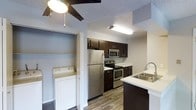 This single-floor residential unit is designed with functionality and modern style in mind. The kitchen is a standout feature, showcasing rich dark espresso cabinetry that contrasts beautifully with light countertops and a clean stainless steel sink. A full suite of stainless steel appliances — including a refrigerator, electric range, and built-in microwave — gives the kitchen a sleek, contemporary feel. The wood-look flooring throughout adds warmth and continuity to the space.

A notable convenience is the in-unit washer tucked neatly into a dedicated closet area, making laundry easily accessible without leaving the home. The ceiling features a ceiling fan with an integrated light fixture, contributing to both comfort and illumination. The textured ceiling adds a subtle architectural detail consistent throughout the unit.

The open sightlines between the kitchen and surrounding living areas create a sense of connected, efficient space that is well-suited for everyday living. Neutral wall tones keep the interior bright and versatile, allowing the darker cabinetry and hardware to serve as defining design accents. Overall, the unit balances practical amenities with a clean, modern aesthetic.