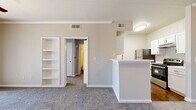 Located at 777 N Air Depot Blvd in Midwest City, Oklahoma, this single-floor, one-bedroom, one-bathroom residence offers a practical and comfortable layout. The combined kitchen and living area serves as the heart of the home, featuring a white peninsula that separates the two spaces while maintaining an open feel. The galley-style kitchen is well-appointed with white cabinetry, white countertops, a stainless steel refrigerator, a range with oven, a dishwasher, and warm wood-look vinyl flooring that adds a clean, modern touch. A standout feature of the living area is a built-in white shelving unit, providing convenient display and storage space. The living room is finished with neutral carpet, creating a soft and inviting atmosphere. A hallway connects the main living space to the private areas of the home, including a dedicated closet for additional storage. The bedroom is a comfortable size, featuring plush carpeting, a ceiling fan with light, and a window with blinds that brings in natural light. The bathroom includes a single vanity with white cabinetry, a large mirror, a tiled shower-tub combination, and wood-look flooring that ties together the home's consistent design aesthetic. Neutral tones throughout give the space a clean, move-in-ready character.