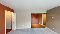 This single-floor unit offers a functional and well-organized layout across two bedrooms, one bathroom, a galley kitchen, and dedicated laundry space. The living area is carpeted in neutral tones and benefits from natural light through a sliding glass door that opens to a private patio. An adjacent dining area features warm hardwood-style flooring and a ceiling light fixture with decorative detailing, visually separating the two spaces.

The galley kitchen is efficiently designed with dark espresso cabinetry lining both walls, granite-style countertops, a stainless steel sink, and black appliances including a gas range, microwave, refrigerator, and dishwasher. The kitchen connects directly to an in-unit laundry room equipped with a full-size washer.

The primary bedroom is generously proportioned, featuring carpet flooring, a window admitting natural light, and a closet. The second bedroom is accented by a bold orange feature wall and carpet flooring. The bathroom includes a tub/shower combination with large-format tile surround, a dark wood vanity with granite-style countertop, and hardwood-style flooring throughout.