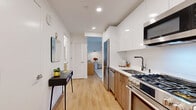 Located at 10-14 LeCount Place in New Rochelle, NY, this thoughtfully designed unit makes efficient use of its compact footprint across a single floor. The galley-style kitchen is outfitted with stainless steel appliances — including a gas range, dishwasher, built-in microwave, and French door refrigerator — complemented by white gloss upper cabinetry, warm wood-toned lower cabinets, and a clean white countertop. Light wood-style flooring runs throughout the entry and kitchen corridor, creating a warm, cohesive flow into the living areas. The bedroom is a standout space, featuring a dramatic floor-to-ceiling window that floods the room with natural light and offers open city views. An eye-catching abstract wallpaper mural adds an artistic focal point, while multiple built-in closets provide generous storage. The full bathroom is finished with marble-style surround tiling in the tub/shower combo, maintaining the unit's clean, contemporary aesthetic. Additional highlights include in-unit laundry and multiple closets throughout. Recessed lighting and crisp white walls enhance the sense of brightness and openness throughout the entire space.