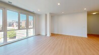 Located on the ninth floor at 8605 Cameron St in Silver Spring, Maryland, this two-bedroom, two-bathroom residence offers a thoughtfully designed single-level layout with a clean, modern aesthetic. Light-toned hardwood flooring runs throughout the main living areas and bedrooms, complementing the crisp white walls and bright, airy atmosphere.

The spacious living room is a standout feature, highlighted by floor-to-ceiling windows that frame sweeping views of the Silver Spring skyline, flooding the space with natural light. Recessed lighting adds a polished finish to the open layout. A well-defined hallway connects the living area to the private quarters, providing a clear and functional flow through the home.

The primary bedroom is generously sized, featuring large windows with city views and ample room for a full furniture arrangement. The second bedroom offers a comfortable, versatile space suitable for guests or a home office. Both rooms benefit from the same consistent light wood flooring and neutral palette.

Each of the two bathrooms showcases stylish, contemporary finishes, including white subway tile surrounds in the shower-tub combinations and distinctive dark herringbone-patterned tile flooring. White vanities with marble-style countertops complete the refined look. The kitchen and hallway round out the efficient and well-organized floor plan of this modern Silver Spring residence.