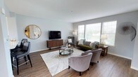 This well-appointed multi-floor residence spans three levels and offers a thoughtfully designed layout with contemporary finishes throughout. The living room serves as a welcoming centerpiece, featuring wide-plank hardwood-style flooring, neutral gray walls, and an abundance of natural light streaming through large windows and a sliding glass door. The open, airy atmosphere is further enhanced by the generous proportions of the space.

The kitchen is both stylish and functional, outfitted with crisp white shaker cabinetry, light quartz countertops, a classic subway tile backsplash, and a full suite of stainless steel appliances including a gas range, built-in microwave, and refrigerator. Pendant lighting adds a refined touch over the kitchen island.

Adjacent to the kitchen, the dining area enjoys access to an outdoor balcony through a sliding glass door, allowing for seamless indoor-outdoor living. The bedrooms offer comfort and tranquility, each featuring plush carpet, soft neutral tones, and windows with outdoor views. The hallways connect the floors gracefully, accented by a decorative pendant light fixture. Bathrooms are clean and modern, with white cabinetry and hardwood-style flooring. Throughout, the residence maintains a cohesive, contemporary aesthetic.