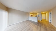 This single-floor unit offers a clean, contemporary layout designed for comfortable everyday living. The open-concept living and dining area is finished with light hardwood-style flooring and neutral warm-toned walls, creating a bright and welcoming atmosphere. A peninsula-style kitchen seamlessly divides the space, equipped with stainless steel appliances including a refrigerator, electric range, and over-the-range microwave. The kitchen features two-tone cabinetry — white uppers paired with rich wood-toned lower cabinets — topped with crisp white countertops and recessed lighting overhead.

The bedroom is generously sized with plush wall-to-wall carpeting, a large window fitted with horizontal blinds for natural light and privacy, and ample wall space for furnishing flexibility. The full bathroom is finished with large-format white floor tiles, a white vanity with modern hardware, a distinctive glass bowl sink, a large mirror, and a tiled shower-tub combination.

A separate living area — or secondary room — features hardwood-style flooring, a window, and sliding glass doors that open to a private balcony overlooking outdoor surroundings, bringing in natural light and a sense of openness. The overall design is clean, minimal, and move-in ready.