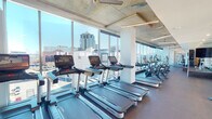 Located at 404 N Eugene St in downtown Greensboro, North Carolina, this fitness center offers a well-appointed, single-level workout space designed with both function and aesthetics in mind. The facility's most striking architectural feature is its expansive floor-to-ceiling glass curtain wall, which floods the interior with natural light and provides panoramic views of the downtown Greensboro skyline, including the neighboring Marriott hotel and surrounding cityscape.

The exposed concrete ceiling with integrated linear LED lighting lends an industrial-modern character to the space, complemented by stacked stone accent walls that add warmth and texture throughout. The cardio zone is lined along the window wall and features a row of Life Fitness treadmills equipped with individual touchscreen monitors, alongside upright and recumbent stationary bikes, ellipticals, and stair climbers—all positioned to take full advantage of the city views.

A dedicated free weights area includes a comprehensive dumbbell rack, medicine balls, stability balls, and large wall-mounted mirrors paired with a flat-screen TV. A functional trainer cable machine station offers versatile strength training options. Rubber flooring throughout provides durability and comfort underfoot. Glass doors in the free weights section open directly to an outdoor pool terrace, seamlessly connecting indoor fitness with outdoor amenities.