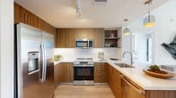 Located in the heart of Miami, this contemporary residence at 934 SW Second Ave offers a thoughtfully designed layout accommodating six bedrooms and two bathrooms across a single floor. The open-concept kitchen and living area serves as the centerpiece of the home, featuring warm walnut-toned cabinetry, stainless steel appliances, a large waterfall-edge island with bar seating, and pendant lighting. Floor-to-ceiling windows flood the living space with natural light while framing sweeping views of the Miami skyline. The living area maintains a clean, neutral palette with light hardwood flooring throughout. Each bedroom is bright and airy, benefiting from large windows with city views; the primary bedroom offers direct access to a balcony overlooking the urban landscape. The two bathrooms are finished in crisp white tile — one features a glass-enclosed walk-in shower with a wood-accented vanity, while the second includes a full soaking tub and shower combination. A dedicated closet provides additional storage. The overall design aesthetic is modern and minimalist, with white walls, clean lines, and natural wood accents creating a cohesive, sophisticated atmosphere ideal for urban living in downtown Miami.