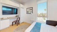 Located on the 7th floor at 3920 W 5th St in Los Angeles, this modern apartment offers a thoughtfully designed single-level layout with clean lines and contemporary finishes throughout. The interior is bathed in natural light, with large floor-to-ceiling windows framing sweeping views of the Los Angeles cityscape, palm tree-lined streets, and open sky — a standout feature visible from both the bedroom and living areas.

The kitchen is outfitted with two-tone cabinetry — crisp white uppers and dark lower units — paired with a white quartz countertop, a classic subway tile backsplash, a matte black pull-down faucet, and stainless steel appliances including a range, dishwasher, and over-the-range microwave. Light hardwood flooring flows through the main living areas, adding warmth to the otherwise minimalist aesthetic.

The bedrooms are bright and well-proportioned, each benefiting from generous window placement and built-in storage solutions. The bathrooms are finished to a high standard, featuring large-format tile, glass-enclosed walk-in showers, wall-mounted vanities with matte black fixtures, and accessibility-friendly grab bars. The overall ambiance is clean, calm, and modern — ideal for urban living in the heart of Los Angeles.