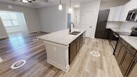 Located at 1220 Strensall Ln in Charlotte, NC, this well-appointed single-story, 2-bedroom, 2-bathroom home showcases a thoughtfully designed open-concept floor plan with modern finishes throughout. The kitchen is a standout feature, boasting a large granite-topped island with a dual-basin undermount sink and matte black faucet, sleek white upper cabinetry, dark lower cabinets, a classic subway tile backsplash, and stainless steel appliances including a range, microwave, and refrigerator with ice maker. Pendant lighting above the island adds a stylish touch. The kitchen flows seamlessly into the living area, which features a distinctive coffered ceiling with a ceiling fan, creating an elegant architectural focal point. Light wood-look flooring extends throughout the main living areas, while plush carpet adds comfort to the bedrooms. The spacious primary bedroom includes a tray ceiling with ceiling fan and a sliding glass door providing access to an outdoor space. Both bathrooms are well-appointed with dual-sink granite vanities, dark cabinetry, matte black hardware, framed mirrors, and light tile flooring. The primary bath offers an elongated layout with a walk-in shower. Two closets provide ample storage. Clean lines, neutral tones, and consistent modern hardware tie the entire home together cohesively.