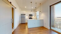 Located at Enclave Piney Lane in Asheville, NC, this single-floor residence offers a clean, modern aesthetic throughout. The heart of the home is an open-concept kitchen and living area finished with warm hardwood flooring. The kitchen is thoughtfully designed with crisp white shaker-style cabinetry extending to the ceiling, a classic subway tile backsplash, and a full suite of stainless steel appliances including a refrigerator, electric range, and built-in microwave. A central island with an integrated sink and pendant lighting in brushed brass finishes serves as both a functional workspace and a casual gathering spot. A barn-style sliding door adds a charming architectural detail to the living space. The bedroom is carpeted for comfort and features access to a spacious walk-in closet with built-in shelving, as well as convenient access to a well-appointed bathroom. The bathroom is finished with a white subway tile tub surround, a single-sink vanity with a clean white countertop, and hardwood-style flooring. Sliding glass doors lead to a private balcony that frames picturesque views of the surrounding Asheville landscape, allowing natural light to fill the interior and connecting the living space to the outdoors.