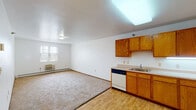 This single-floor unit offers a practical and well-organized layout designed for comfortable everyday living. The open-concept main area seamlessly connects the living space and kitchen, with light wood-style flooring in the kitchen zone transitioning to neutral carpet in the living area. The kitchen is equipped with warm oak-toned cabinetry providing ample upper and lower storage, a built-in dishwasher, an electric range, a refrigerator, and a single-basin sink. A skylight-style ceiling fixture brightens the kitchen, while a window allows natural light into the living area. A wall-mounted HVAC unit and baseboard heating ensure year-round climate control.

The bedroom is a well-sized, carpeted retreat featuring a window with outdoor views, baseboard heating, and direct access to a closet with built-in shelving. An accessible bathroom is thoughtfully designed with grab bars, a wall-mounted sink, a medicine cabinet, and wood-style flooring, making it suitable for a range of mobility needs. The entryway connects the living area to the front door via a short, open corridor with wood-style flooring, completing the efficient and functional flow of this single-level unit.