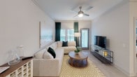 This single-story residence offers a thoughtfully designed layout with multiple bedrooms, a well-equipped kitchen, and multiple bathrooms, all finished in a cohesive neutral palette with coastal-inspired accents. The living room serves as the central gathering space, featuring crown molding, a ceiling fan, and multiple windows with plantation shutters that allow ample natural light. A large sectional sofa anchors the room alongside a round wooden coffee table and a patterned area rug.

The kitchen is outfitted with dark lower cabinetry contrasted by white upper cabinets, granite countertops, a stainless steel refrigerator with ice and water dispenser, a subway tile backsplash, and pendant lighting. A built-in wine rack adds a distinctive architectural touch.

Each bedroom features plush carpet flooring, ceiling fans, plantation shutters, and generous closet access. The primary bedroom connects to a full en-suite bathroom complete with a granite-topped double vanity, dark cabinetry, a glass-enclosed walk-in shower, and a spacious walk-in closet with built-in shelving. A secondary bathroom includes a full soaking tub with a tiled surround. Throughout the residence, light wood-style flooring, crown molding, and consistent neutral tones create a cohesive and comfortable ambiance.
