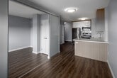 Located at 213 Main St in Toronto's Main Street neighbourhood, this compact yet thoughtfully designed unit offers a clean, modern aesthetic throughout its single floor. Warm hardwood-style laminate flooring runs continuously across all areas, complementing the crisp white walls and creating a cohesive, contemporary feel.

The kitchen is a standout feature, outfitted with two-tone cabinetry — natural wood lower cabinets paired with high-gloss white upper cabinets — white subway tile backsplash, white quartz countertops, and a full suite of stainless steel appliances including a refrigerator, stove, built-in microwave, and dishwasher. The layout is efficient and well-organized, maximizing every inch of space.

The two living areas are open and bright, with large windows fitted with roller shades that allow for both natural light and privacy. A sliding glass door leads to an outdoor balcony access point, offering views of the surrounding neighbourhood. Baseboard heating units are present throughout.

The bathroom is finished in a clean, minimalist style with a soaking tub and shower combo, a wood-toned vanity with a white sink, and a large mirror with integrated lighting. White walls and wood-look flooring maintain the consistent design language found throughout the unit.