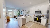 This thoughtfully designed one-bedroom, one-bathroom unit offers an efficient and modern single-floor layout with clean lines and contemporary finishes throughout. The open-concept kitchen flows seamlessly into the living area, creating a cohesive and functional space. The kitchen features white shaker-style cabinetry extending to the ceiling, quartz countertops, a peninsula with bar seating, stainless steel appliances including a refrigerator, electric range, microwave, and dishwasher, and matte black pendant lighting and fixtures. Light wood-style flooring runs throughout the unit.

The living room receives generous natural light through large windows and a glass door that opens to a balcony, with ceiling fans present in both the living room and bedroom. The bedroom is a comfortable size, accommodating a full suite of furniture, and features windows with outdoor views. It connects to a dedicated walk-in closet with built-in shelving, hanging rods, and open cubbies for organized storage.

The bathroom is well-appointed with a wide vanity topped with quartz, a single undermount sink, matte black fixtures, a linen tower cabinet, and a full soaking tub with a tiled surround. Light wood flooring and neutral tones carry through, reinforcing the unit's clean, modern aesthetic.
