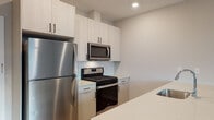 This well-designed two-story residence offers a clean, modern aesthetic throughout its thoughtfully laid-out spaces. The main level features an open-concept kitchen equipped with stainless steel appliances, including a gas range, over-the-range microwave, and full-size refrigerator. Light-toned flat-panel cabinetry reaches toward the ceiling for ample storage, while a white subway tile backsplash adds a classic detail. A generous quartz-topped island with an undermount sink anchors the kitchen, providing both workspace and casual seating potential. The living area on the main floor is bright and welcoming, with large windows that invite natural light and light-toned hardwood-style flooring that carries throughout. A convenient half bath on this level features a modern vanity with clean lines and a large mirror. Upstairs, the bedrooms are carpeted for comfort, each benefiting from natural light through sizable windows. The upper-level bathrooms are finished with contemporary floating vanities, hardwood-style tile flooring, and a glass-enclosed shower, reflecting the same modern sensibility found throughout the home. A staircase connects both floors, and the overall neutral color palette creates a calm, cohesive atmosphere ideal for a variety of living arrangements.