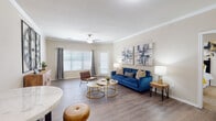 This single-story residence offers a thoughtfully designed layout that balances comfort and functionality. The living room serves as the centerpiece of the home, featuring wood-look flooring, crown molding, and a ceiling fan. Large windows dressed with blinds and curtain panels allow generous natural light to fill the space, creating a bright and welcoming atmosphere.

A dedicated dining or flex area adjoins the living space, providing additional room for entertaining or everyday use. The kitchen is outfitted with white cabinetry, granite-style countertops, and stainless steel appliances including a refrigerator, range, microwave, and dishwasher. Wood-look flooring continues throughout, adding visual continuity.

The bedroom is a well-proportioned retreat with carpeted flooring, built-in shelving, and a dedicated workspace area. The space is designed to accommodate both rest and productivity comfortably.

Two bathrooms serve the residence, each featuring white vanity cabinetry with granite-style countertops, tub-shower combinations with tiled surrounds, and wood-look flooring. Overall, the home maintains a consistent neutral palette with clean finishes, offering a versatile backdrop adaptable to a variety of interior styles.