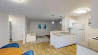 Located in Stonecrest, GA, this single-floor unit offers a well-designed, open-concept layout that seamlessly connects the main living areas. The kitchen is outfitted with white cabinetry, granite-style countertops, a peninsula with a built-in sink and dishwasher, and white appliances including a range and refrigerator. Pendant lighting over the peninsula provides functional illumination while enhancing the kitchen's clean aesthetic. Wood-look flooring flows throughout the main living areas, creating a cohesive and easy-to-maintain surface. The living room is an open, comfortable space accented by contemporary artwork in teal tones, while a dedicated dining area sits adjacent, bathed in natural light from large windows fitted with blinds. A ceiling fan adds comfort to the dining nook. The bedrooms are carpeted for warmth and feature generous natural light from multiple windows. The primary bedroom includes direct access to a private bathroom as well as a walk-in closet. Textured ceilings are present throughout, and the neutral white walls provide a versatile backdrop. The overall layout, as seen in the dollhouse view, is thoughtfully organized to maximize flow and functionality across all spaces.