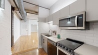 Located in the heart of downtown Houston, this loft-style unit at 909 Texas Ave showcases a compelling mix of historic industrial character and contemporary upgrades. The main living area is an open, airy space defined by warm hardwood floors, exposed brick walls, and original structural beams overhead. Visible ductwork and a ceiling fan with light fixture contribute to the loft's industrial aesthetic, while large windows allow natural light to pour in and offer views of the surrounding urban landscape.

The kitchen is efficiently designed with gray flat-front cabinetry, white subway tile backsplash, and light quartz countertops. Stainless steel appliances — including a range, over-the-range microwave, and refrigerator — are complemented by a black dishwasher and a single-basin sink. A sliding barn door separates the kitchen from the living area, reinforcing the industrial design theme.

The bathroom features a clean, modern aesthetic with a blue-gray vanity, quartz countertop, framed mirror, and matte black hardware accents. A glass-enclosed walk-in shower with white subway tile adds a polished touch, and large-format floor tiles complete the space. Additional rooms include a closet and a utility room, rounding out a well-appointed and functional floor plan in a distinctive downtown setting.