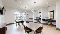 Located at 2901 Indiana St in Dallas, Texas, this contemporary community dining room offers a well-appointed and versatile gathering space designed for both socializing and productivity. The room features light hardwood flooring throughout, crisp white walls, and a bright, open layout that creates an inviting atmosphere.

At the heart of the space are multiple square dining tables paired with modern mid-century-style chairs in dark upholstery with warm wood legs, providing comfortable seating for small groups. Overhead, a striking sputnik-style chandelier serves as a focal point, complemented by recessed lighting that ensures the room is well-lit throughout.

A built-in workstation along one wall includes desktop computers, offering a convenient business center function within the same space. Adjacent dark cabinetry provides additional storage, while a wall-mounted flat-screen TV adds a multimedia element. Colorful abstract artwork adorns the walls, lending the room a creative and vibrant character.

Large sliding glass doors along one wall flood the interior with natural light and provide views of an outdoor area, seamlessly connecting the interior to the exterior environment. A dedicated credenza and additional framed artwork further enhance the polished, curated aesthetic of this functional and stylish community space.